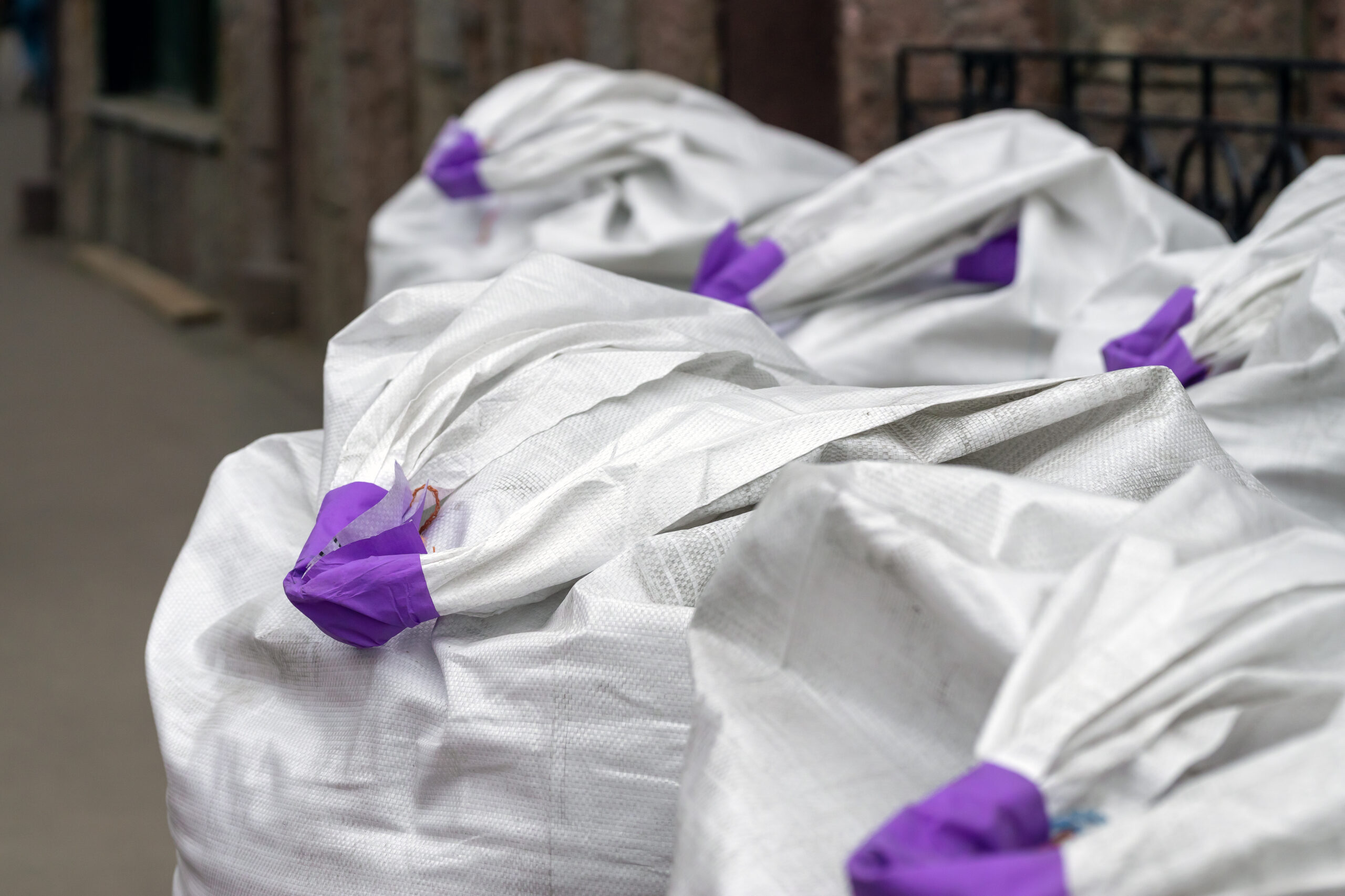 Synthetic white bags with purple handles for building bulk materials. They stand in a row. Many.